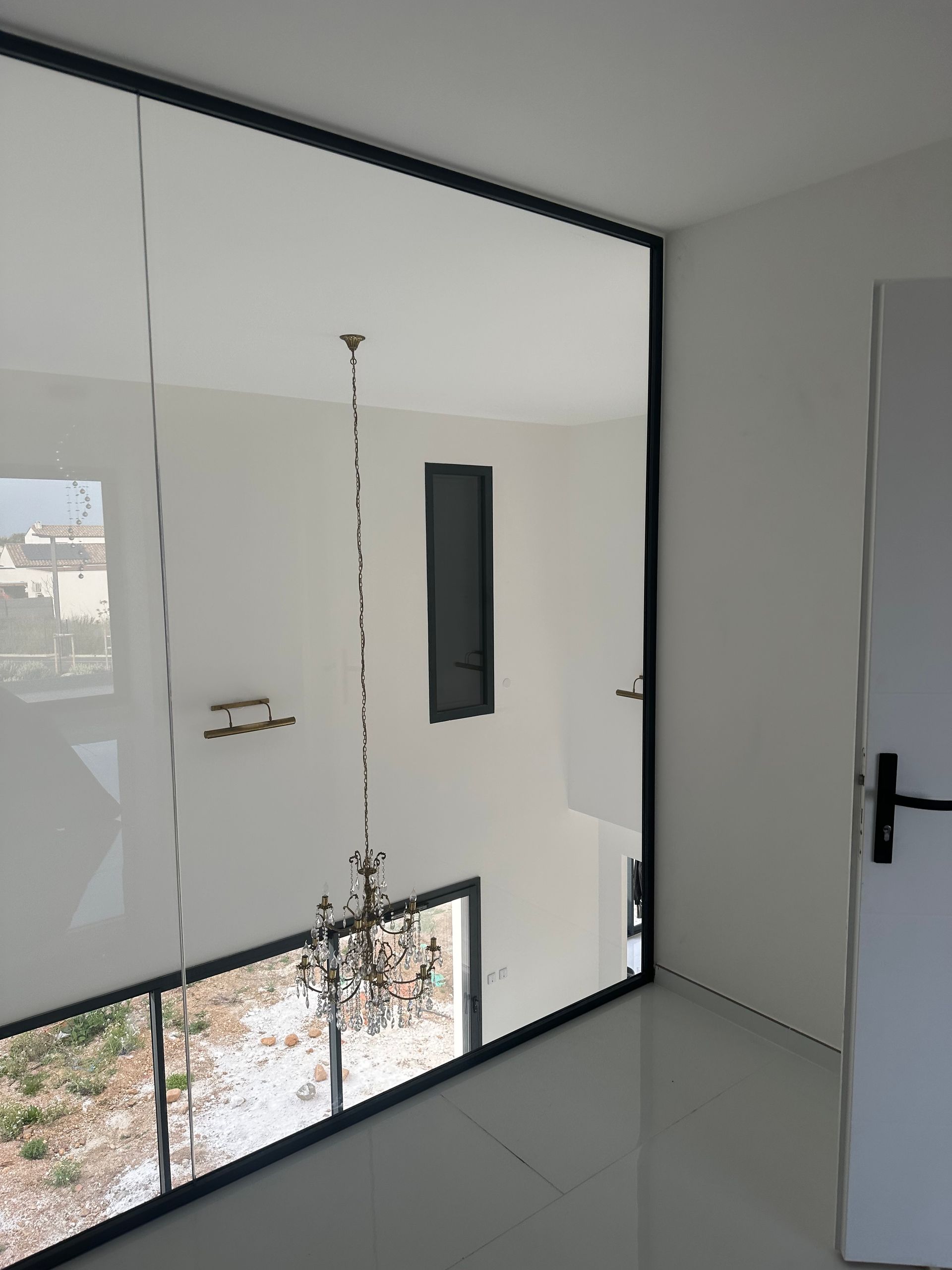 Vue intérieure d'une maison moderne avec une grande baie vitrée, des finitions noires et un lustre.