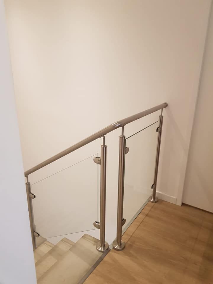 Escalier avec rampe en acier inoxydable et en verre. Sol en bois clair et murs blancs.