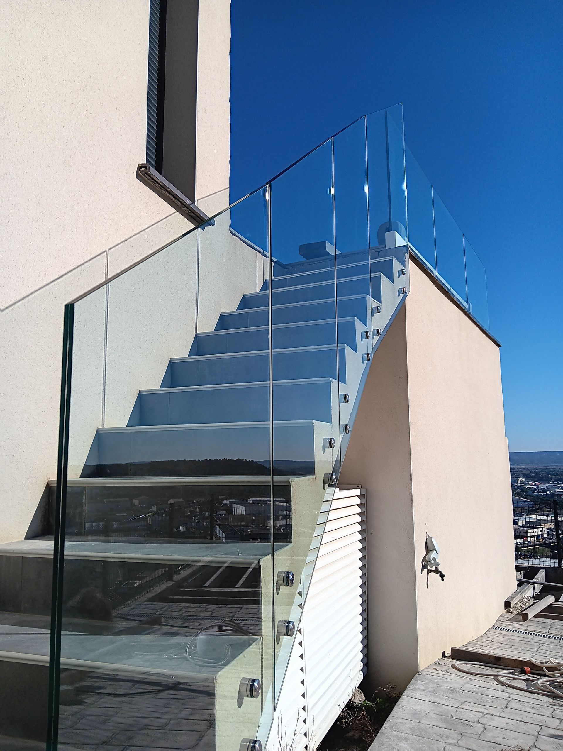 Escalier extérieur avec rambarde et contremarches en verre, ciel bleu en arrière-plan.