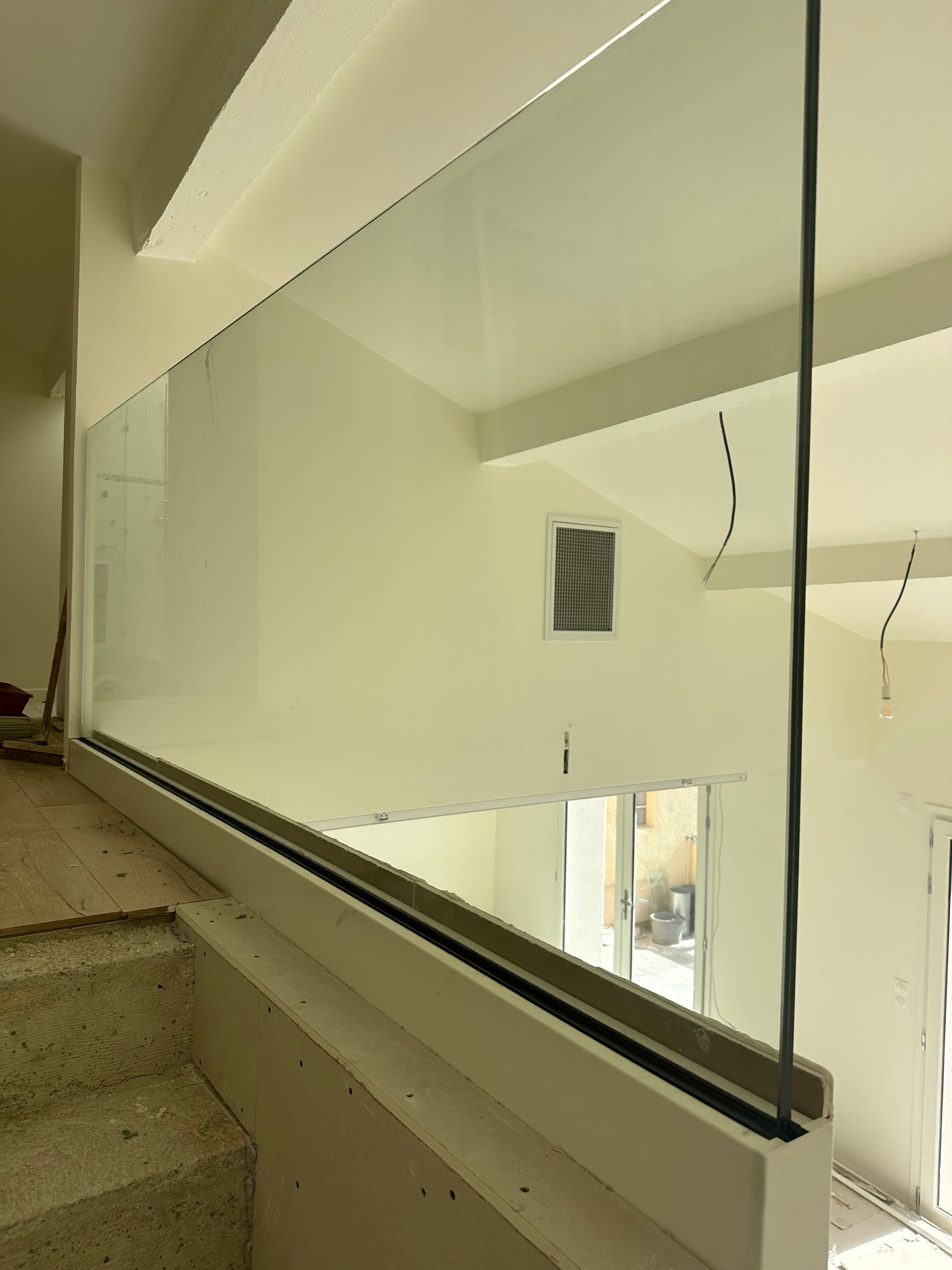 Rambarde en verre sur un escalier dans un bâtiment aux murs blanc cassé.