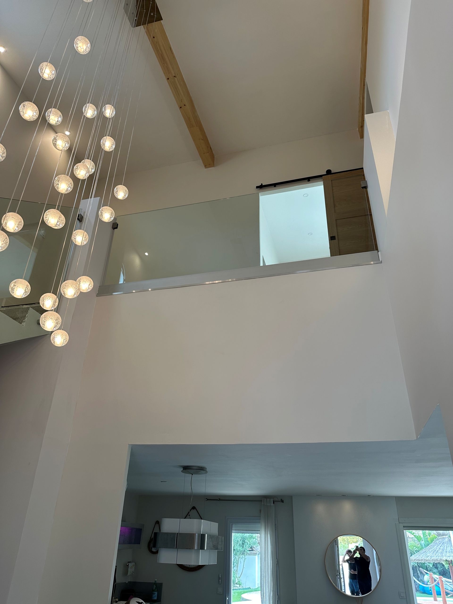 Vue intérieure d'une maison moderne avec de hauts plafonds, une balustrade en verre et un grand lustre.