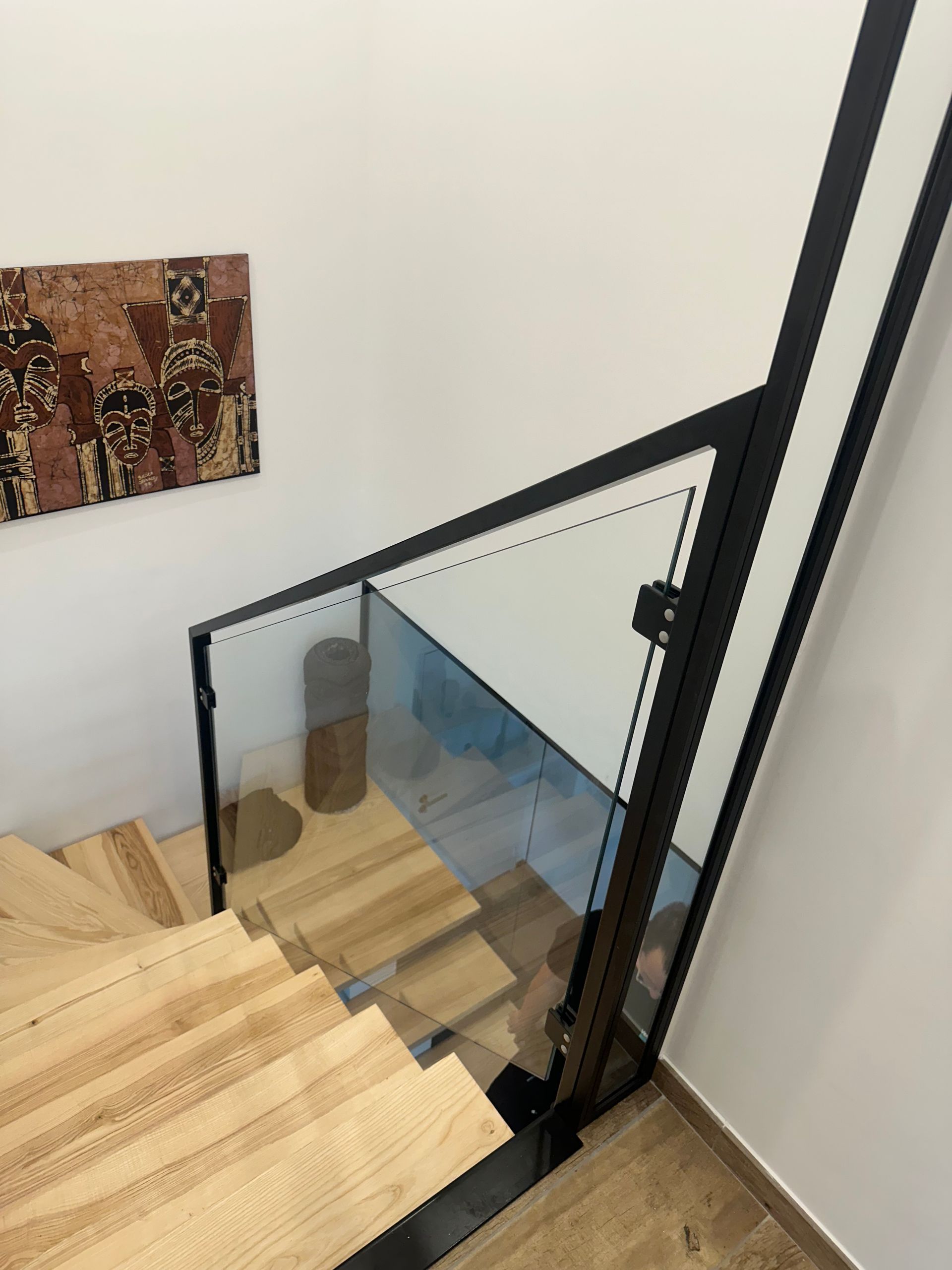 Escalier en bois avec rampe en verre et métal noir, descendant vers le bas. Œuvre d'art au mur.