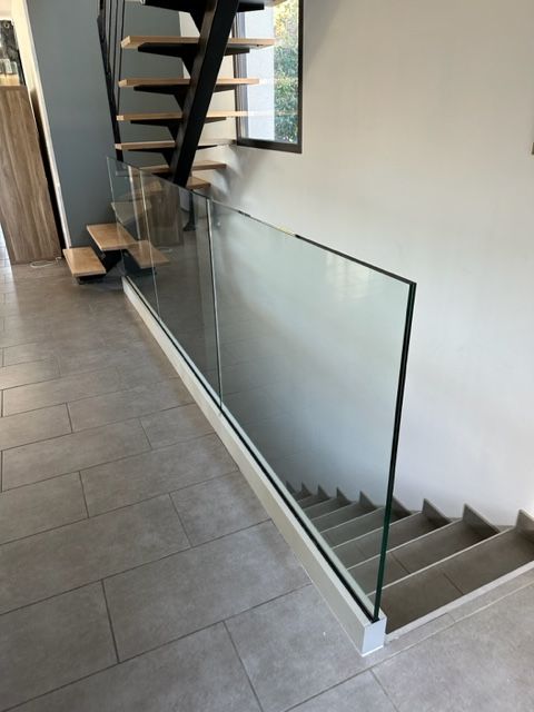 Intérieur moderne avec escalier, balustrade en verre et sol carrelé.