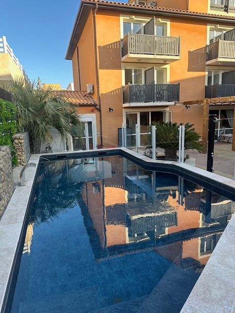 Piscine reflétant un immeuble à balcons. Extérieur lumineux, journée ensoleillée.