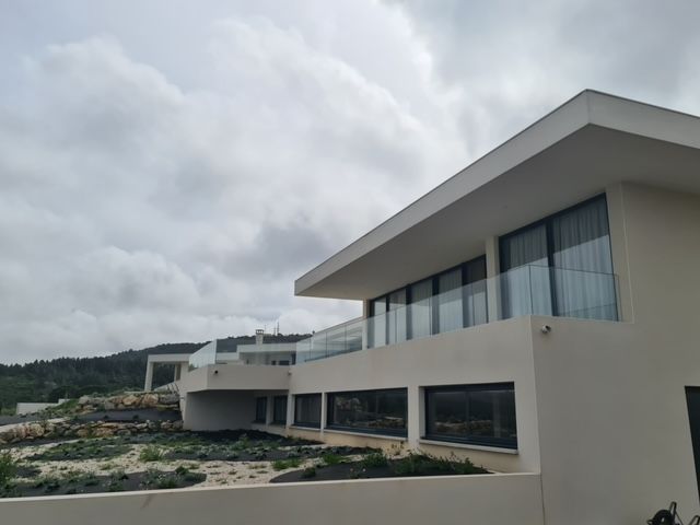 Immeuble blanc moderne avec balcons en verre, sous un ciel nuageux.