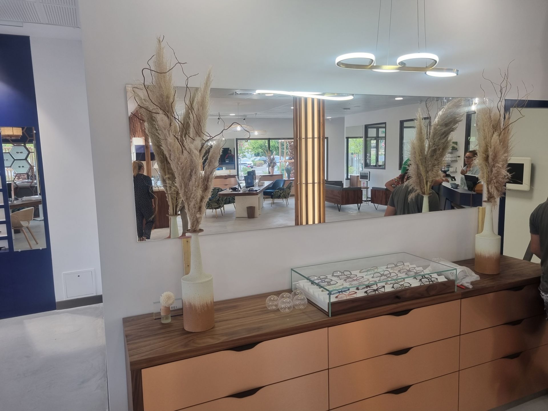 Un long miroir rectangulaire surplombe une commode en bois ornée d'herbes de la pampa, reflétant une pièce lumineuse.