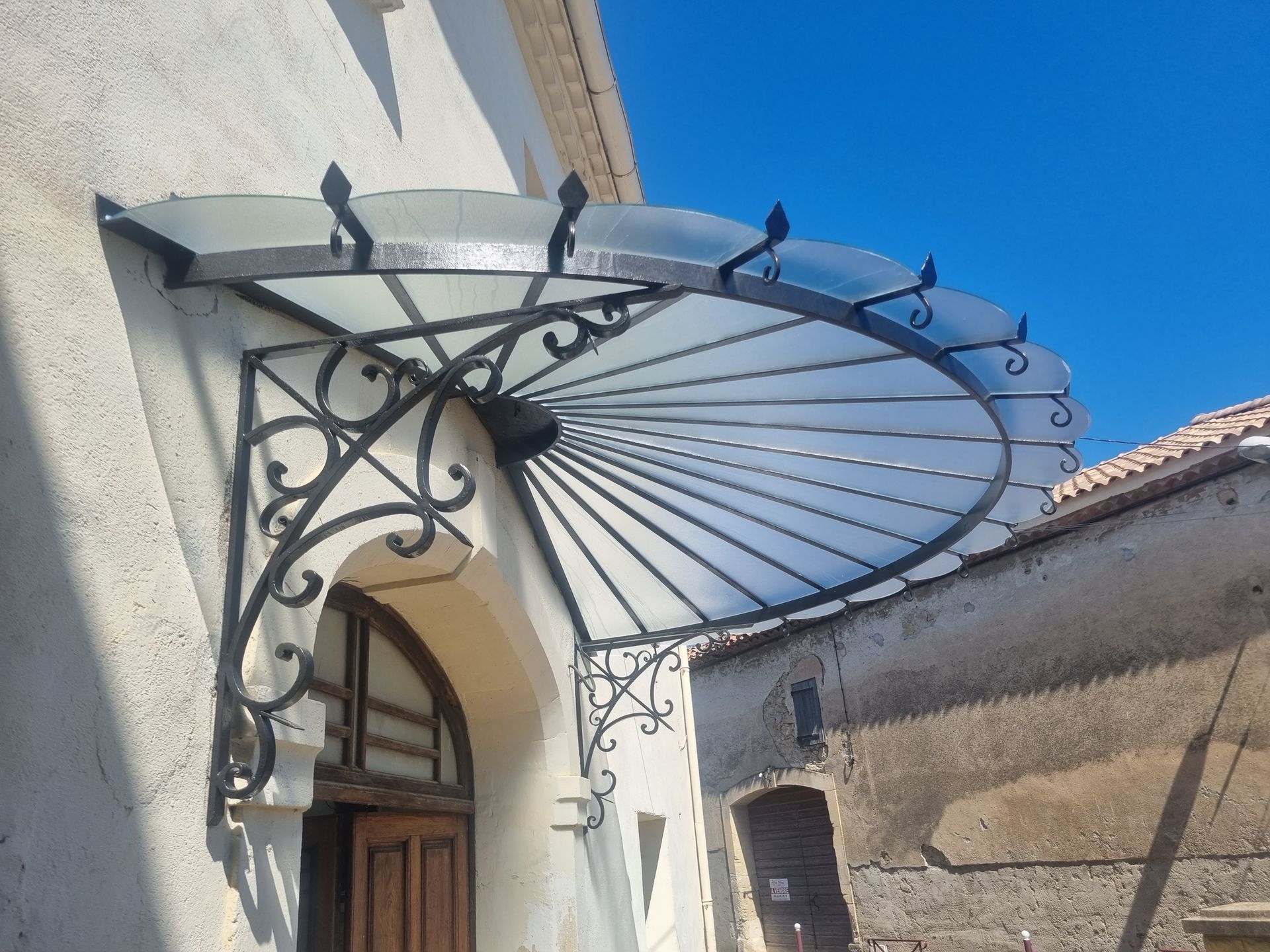Auvent en fer forgé noir et en verre au-dessus d'une porte en bois sur un bâtiment en stuc.