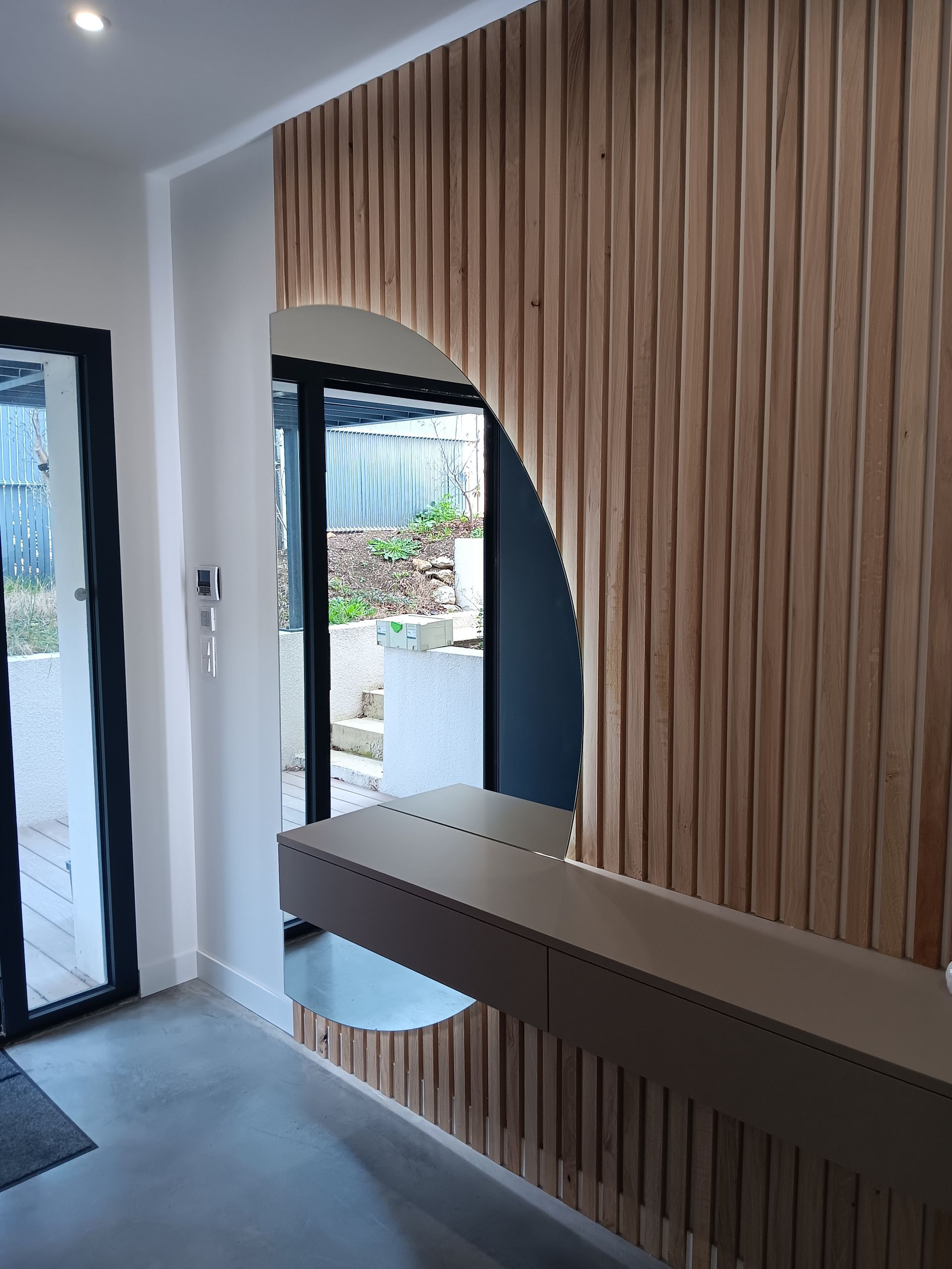Cloison en lattes de bois avec ouverture cintrée, bureau et porte vitrée.