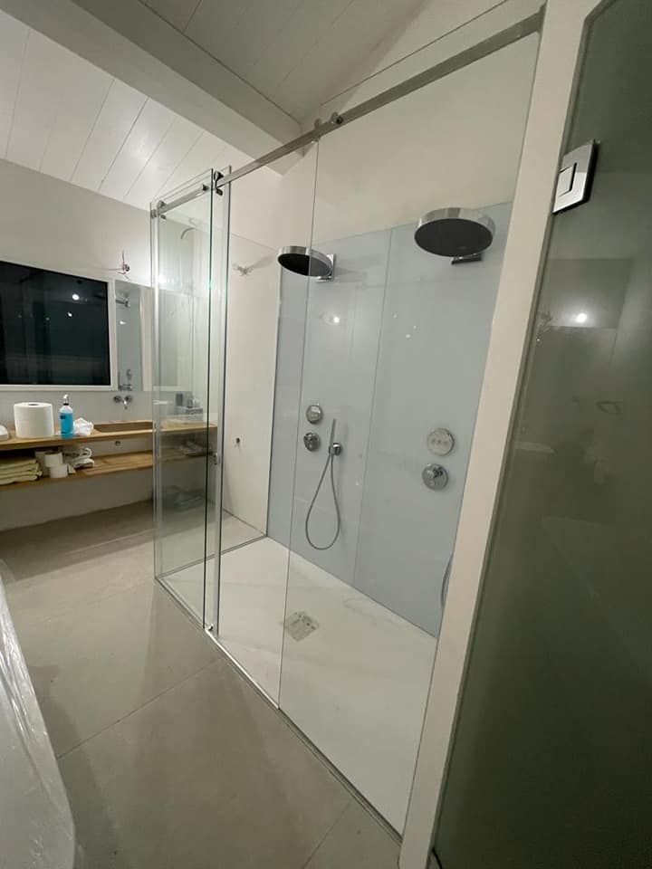 Douche moderne avec parois en verre, pommeau de douche effet pluie et robinetterie chromée. Tons blancs et gris.