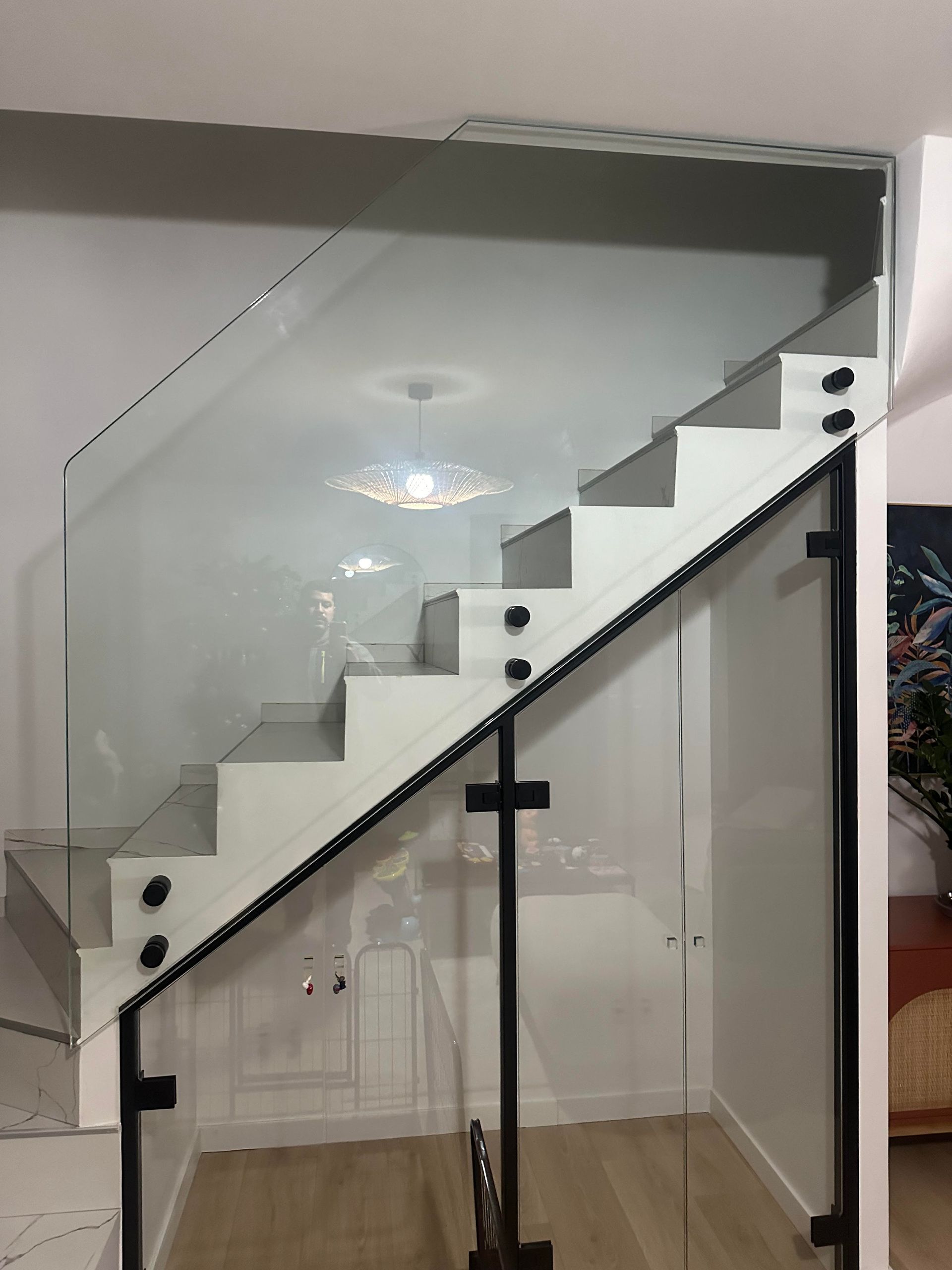 Escalier moderne avec marches blanches et rambarde en verre fixée par des poteaux noirs.