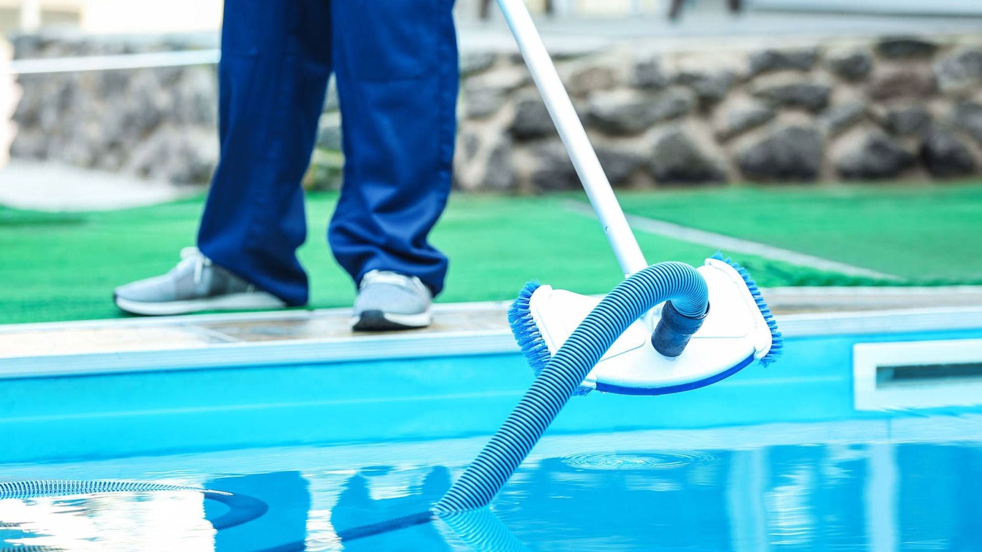 Un hombre está limpiando una piscina con un trapeador.
