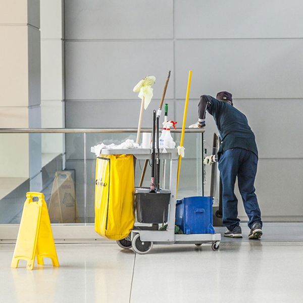 Un hombre está limpiando un piso junto a una señal de precaución amarilla.