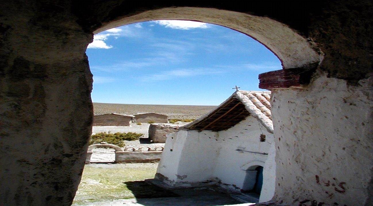Vista de edificios blancos a través de una puerta arqueada, bajo un cielo azul brillante.