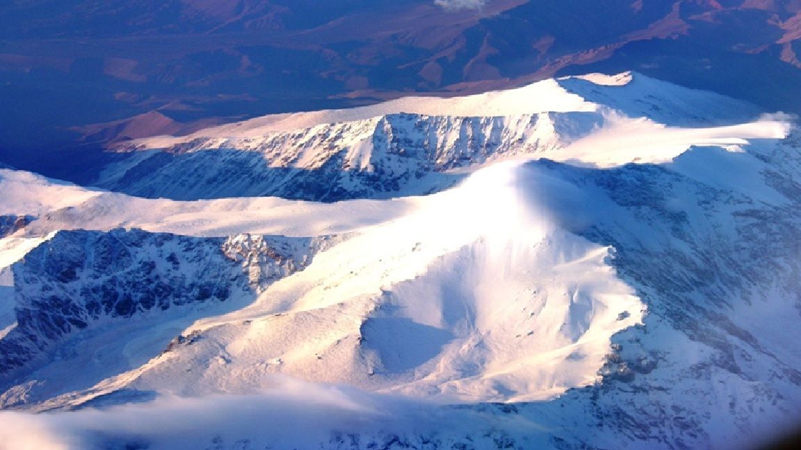 Cordillera cubierta de nieve, bañada por la luz del sol, con un cielo nublado.