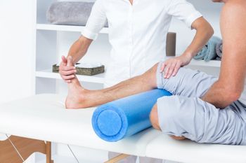 Physio-Behandlung mit Rolle, bei der der Therapeut den Fuß des Patienten biegt