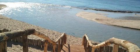 Vista dalle scale di legno che conducono a una spiaggia sabbiosa dove l'acqua sfocia nell'oceano.