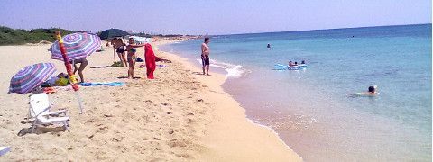 Scena di spiaggia con persone, ombrelloni e acqua limpida.