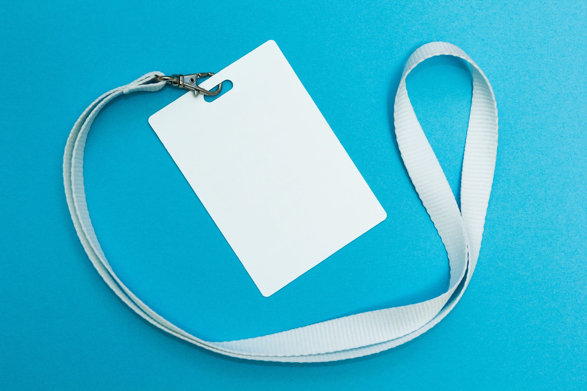 Badge d'identification blanc vierge avec cordon gris, posé sur une surface bleue.