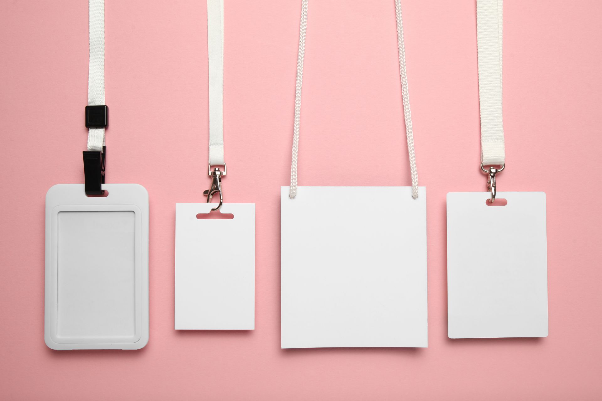 Quatre badges d'identification blancs vierges sont accrochés sur un fond rose.
