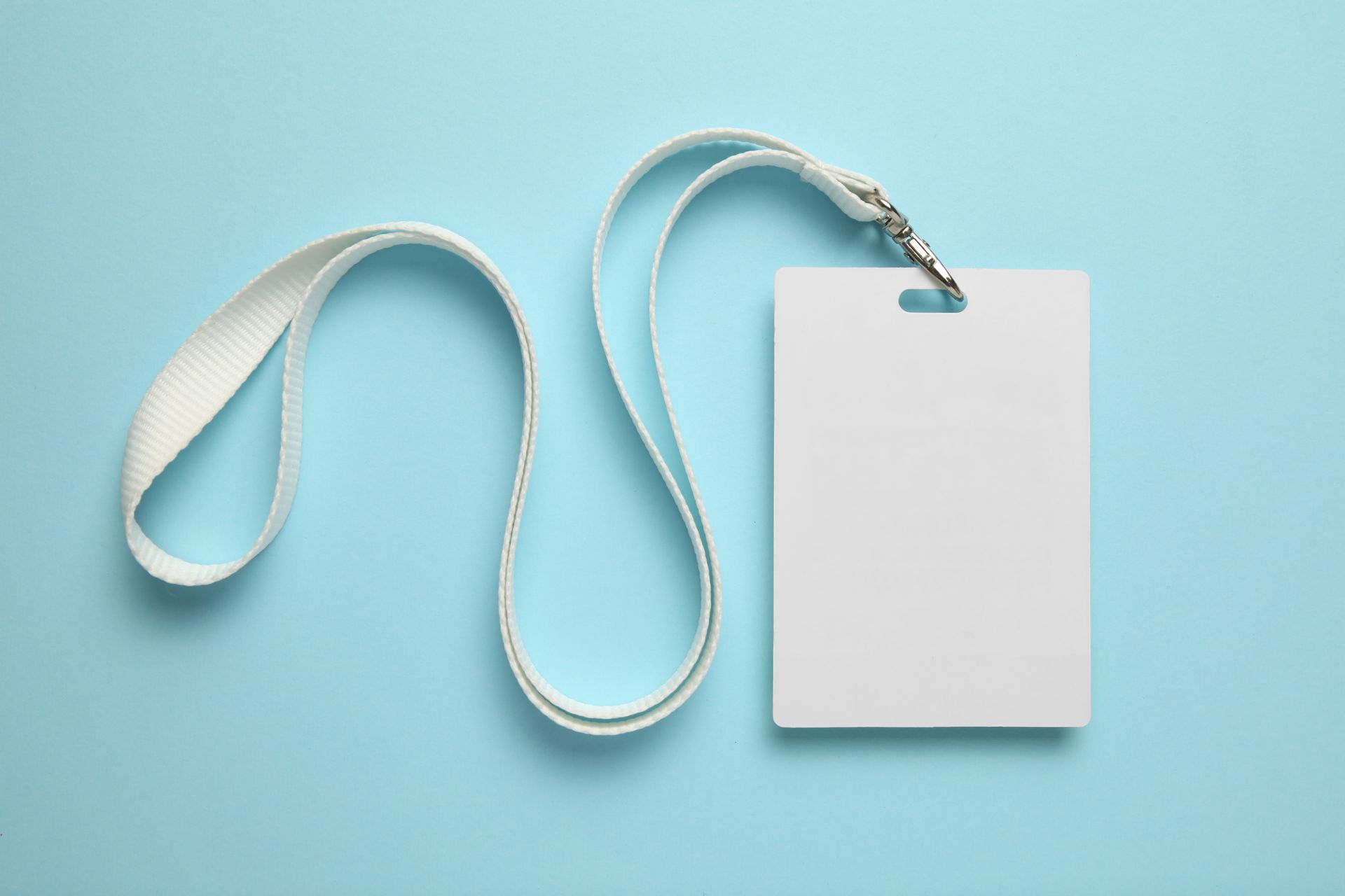 Badge d'identification blanc vierge sur un cordon blanc, posé sur un fond bleu clair.