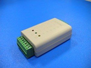 Petit appareil gris avec bornier vert et trois voyants lumineux, sur une surface bleue.