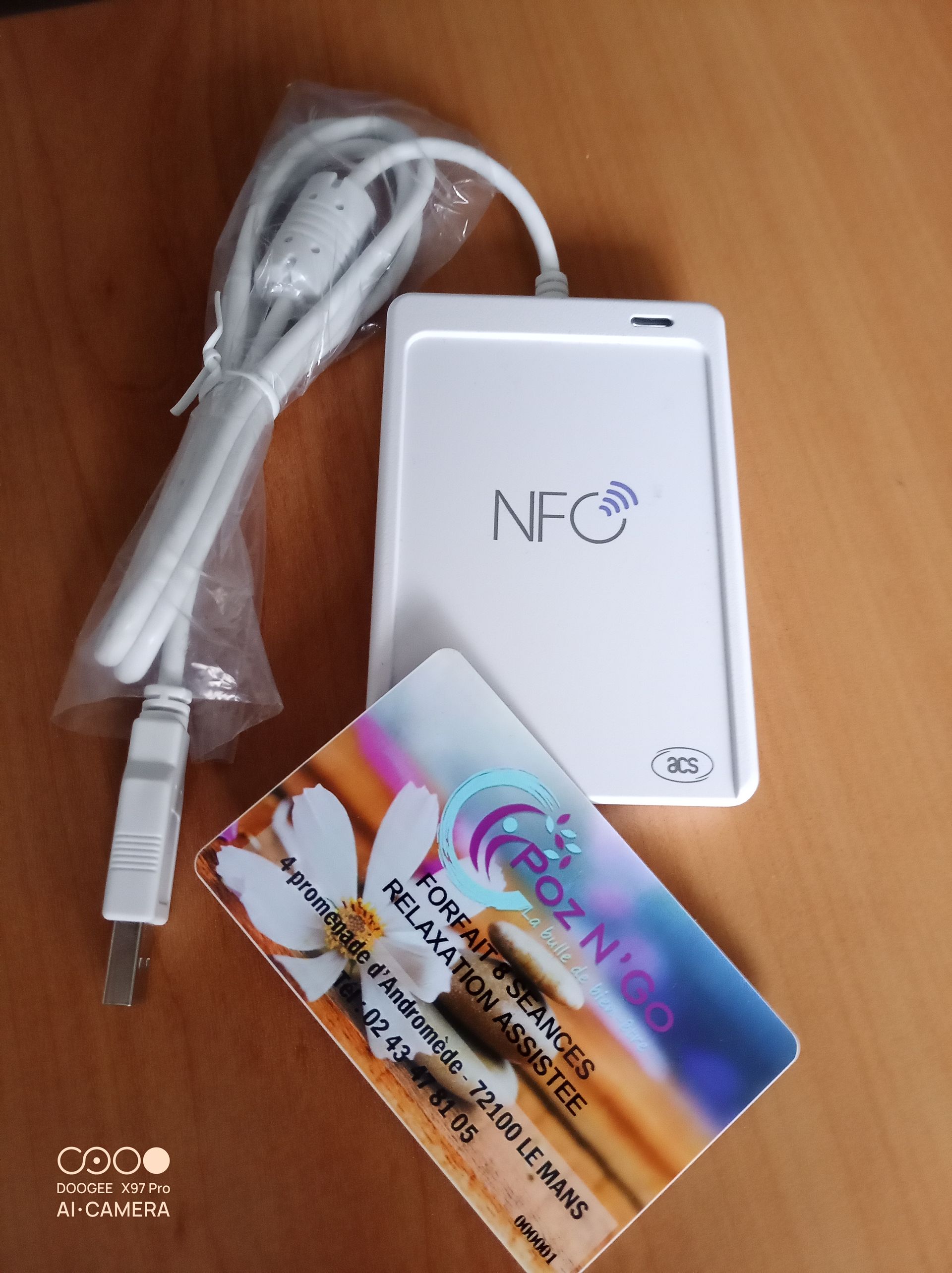 Lecteur de cartes NFC blanc avec câble USB et carte promotionnelle sur une surface en bois.