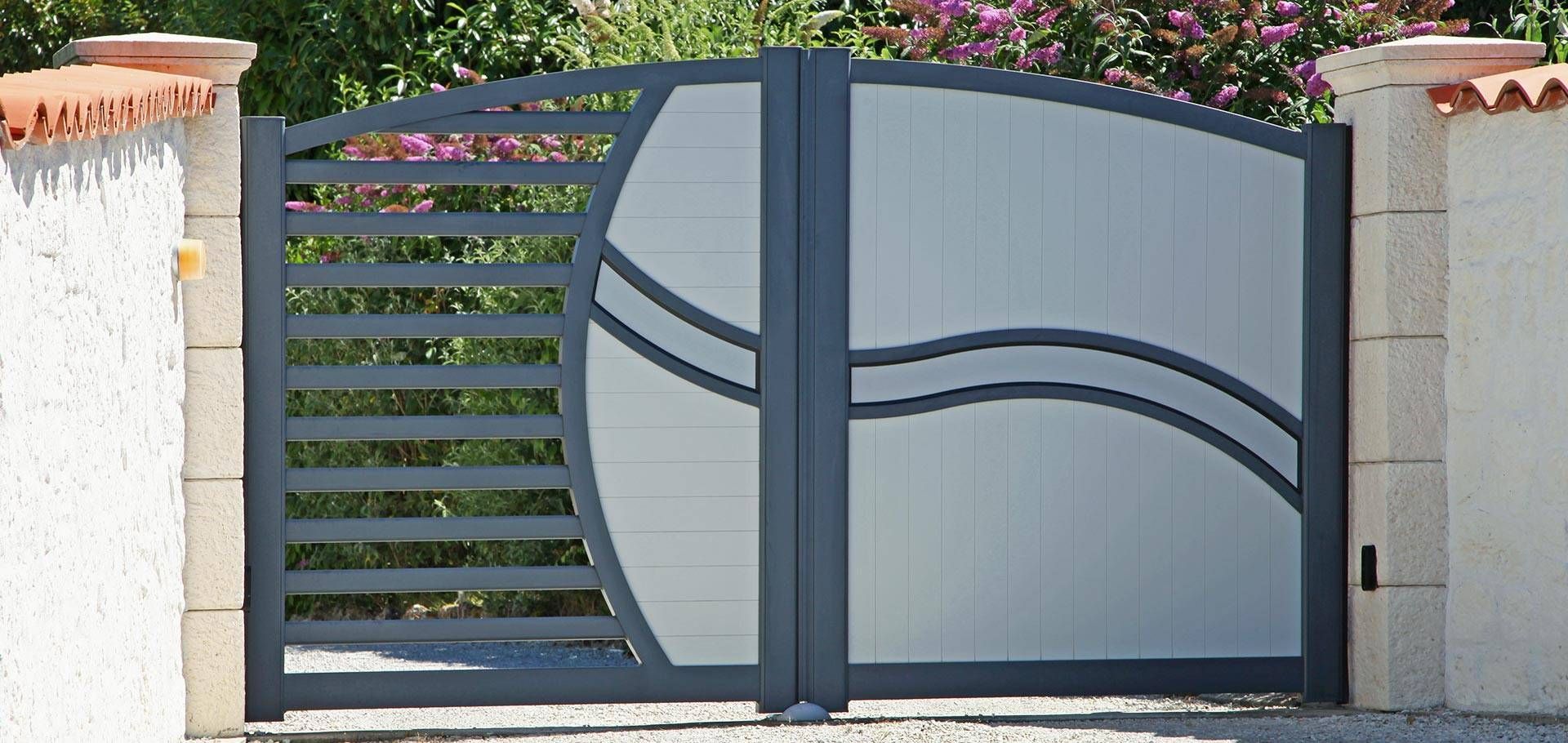 Portail d’allée moderne en métal gris, avec des lignes décoratives incurvées entre des piliers en pierre