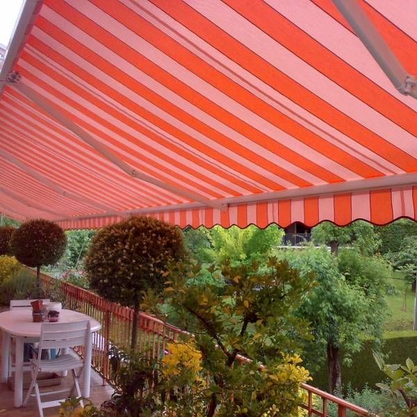Terrasse extérieure sous un auvent à rayures rouges et blanches, avec une table et des chaises blanches donnant sur un jardin verdoyant