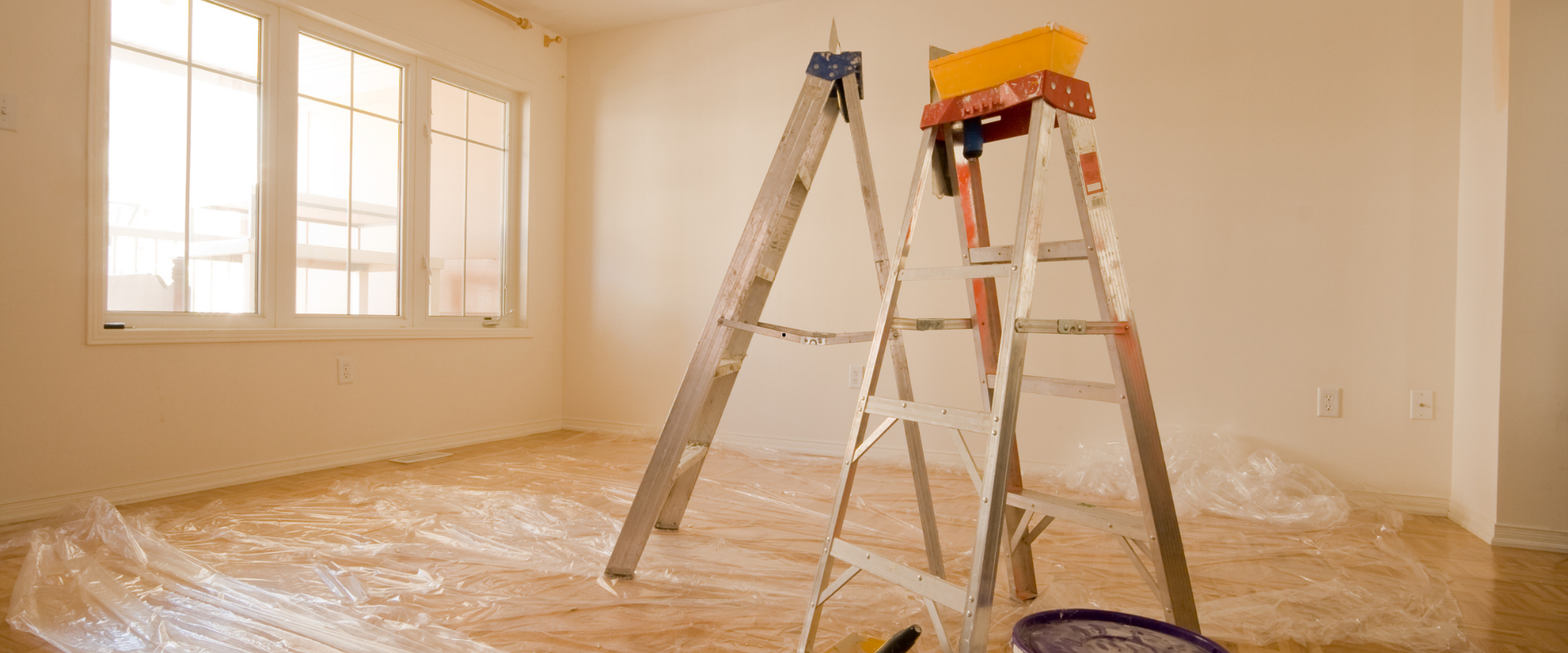 Deux échelles dans une pièce, du matériel de peinture au sol, des fenêtres en arrière-plan.