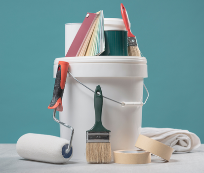 Un seau de peinture blanc rempli de matériel de peinture, de pinceaux, d'un rouleau et d'échantillons de couleurs.