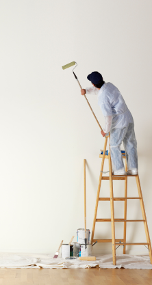 Une personne peint un mur blanc au rouleau, debout sur une échelle en bois. Des pots de peinture sont posés en dessous.