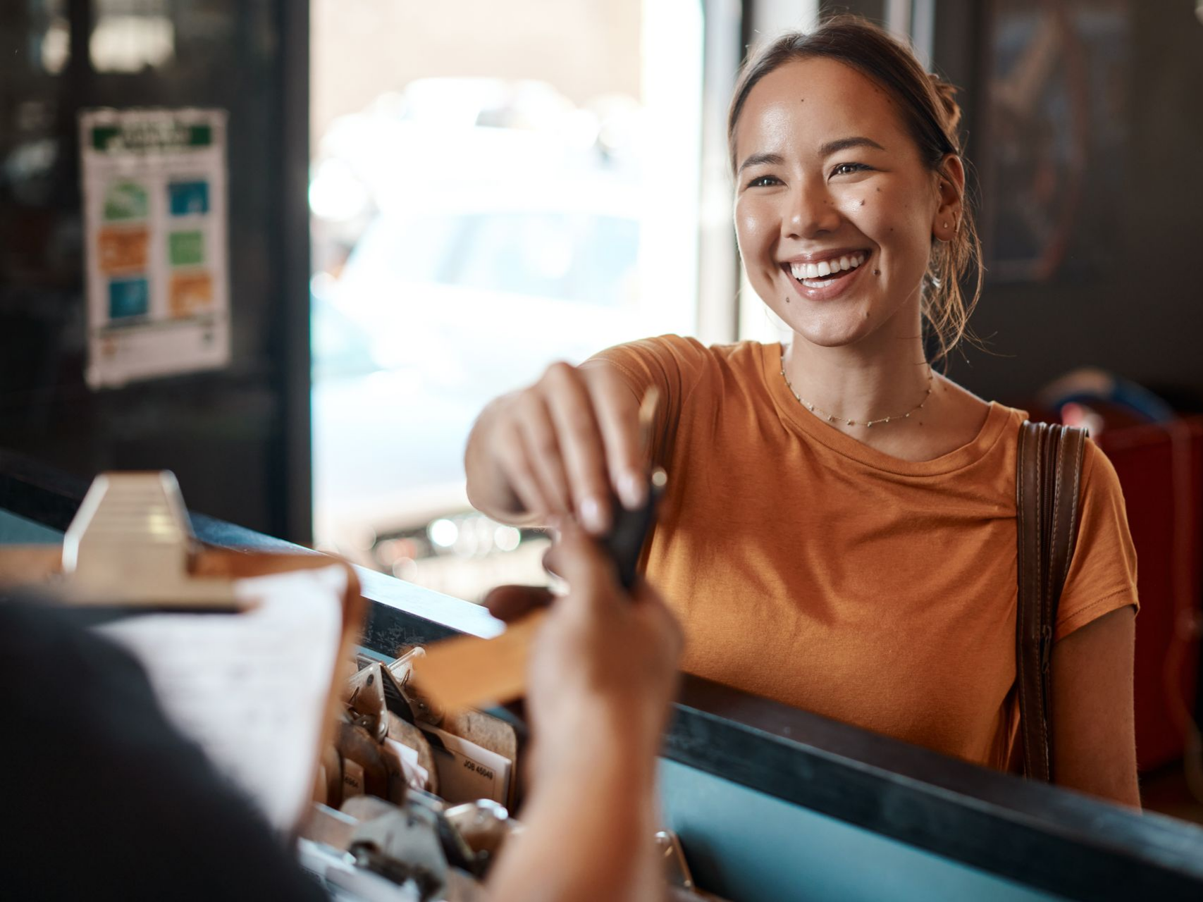 Une femme sourit en tendant des clés à quelqu'un de l'autre côté d'un comptoir.