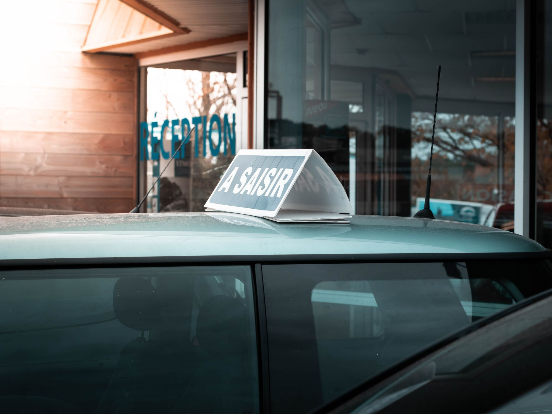 Une voiture avec un panneau triangulaire À SAISIR sur son toit garée devant un bâtiment.