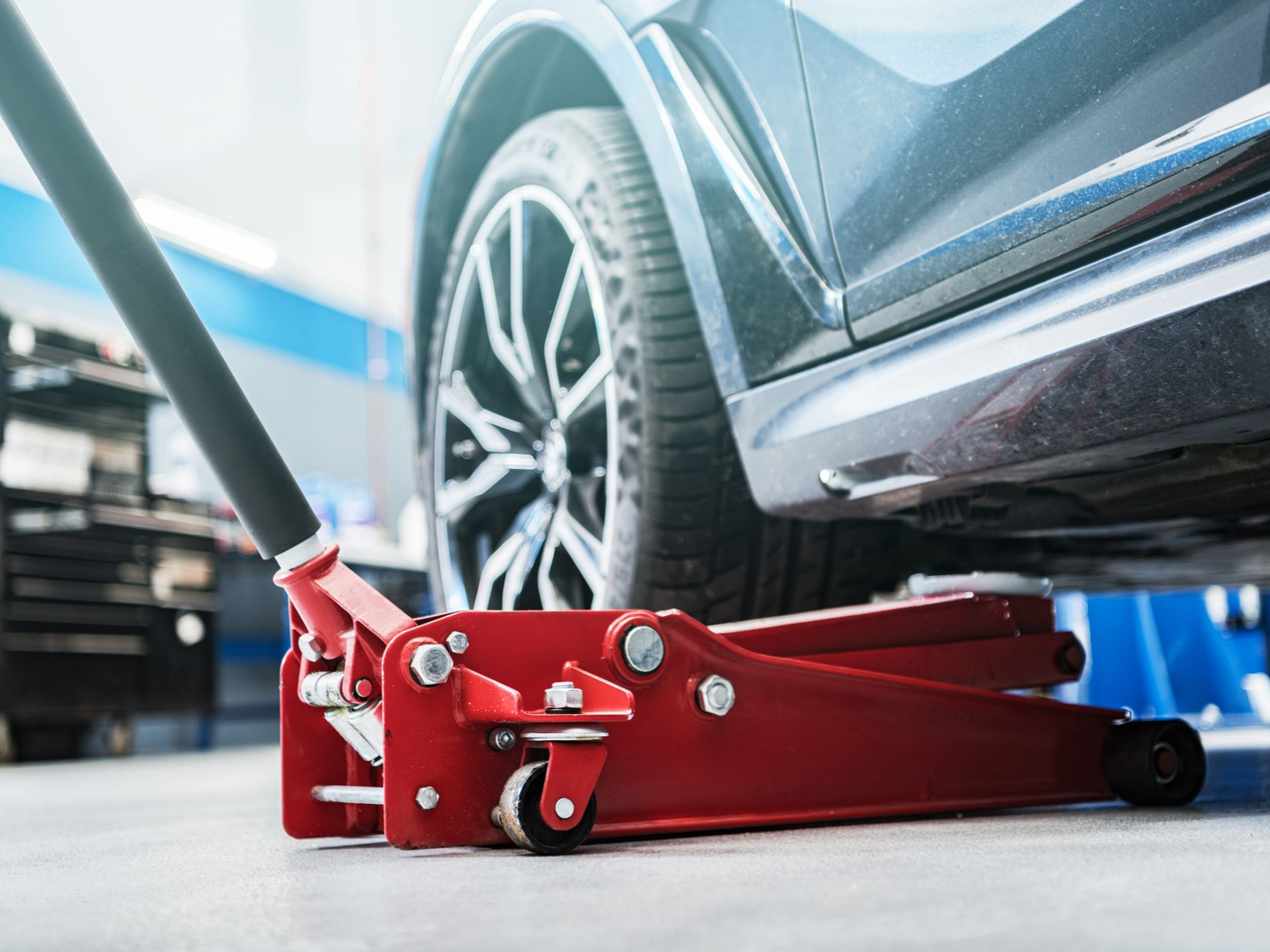 Un cric hydraulique rouge soulève une voiture dans un atelier automobile.