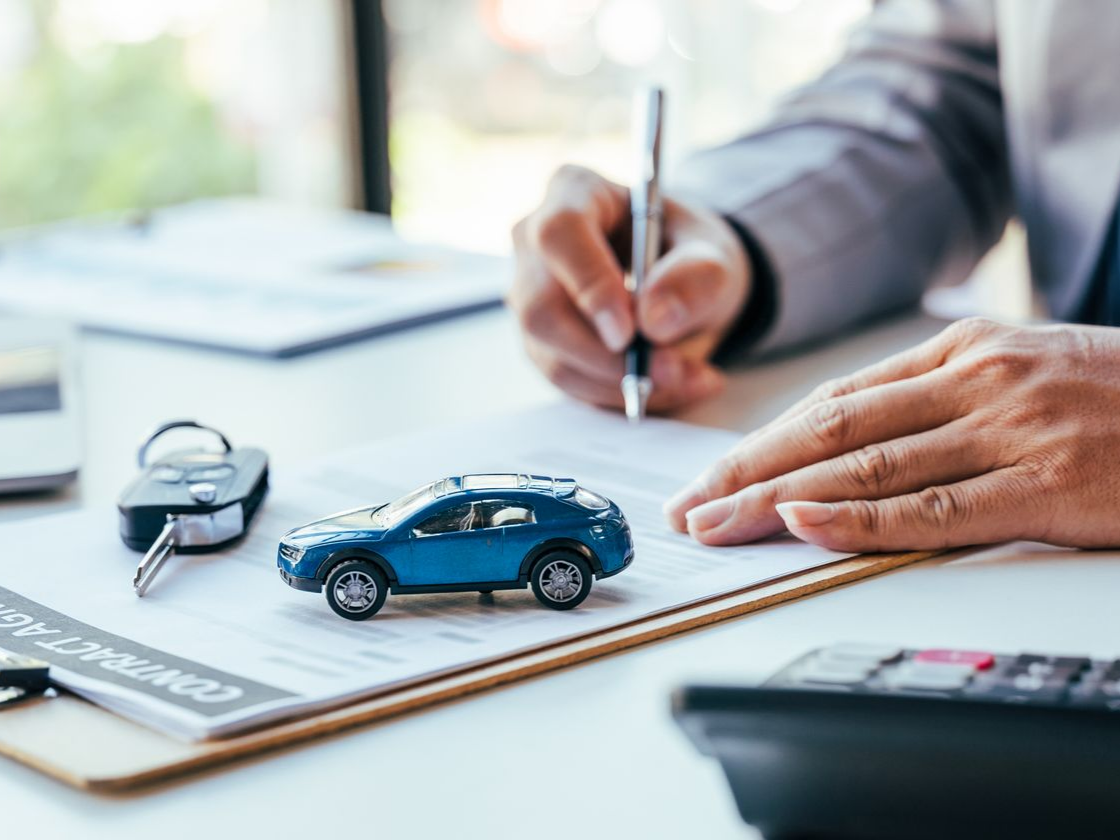 Une personne signant un contrat d'achat de voiture et les clés posées sur le bureau.