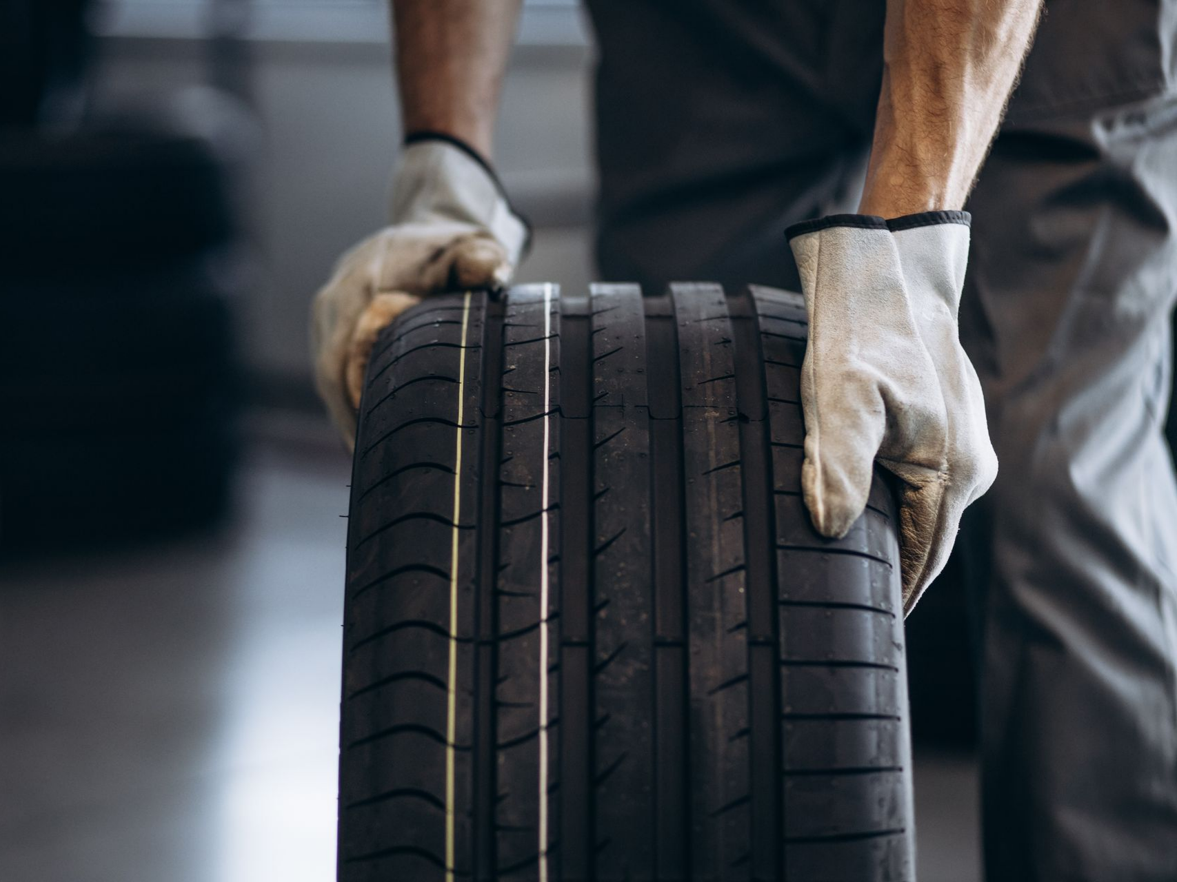 Dans un garage, un mécanicien portant des gants tient un pneu neuf.