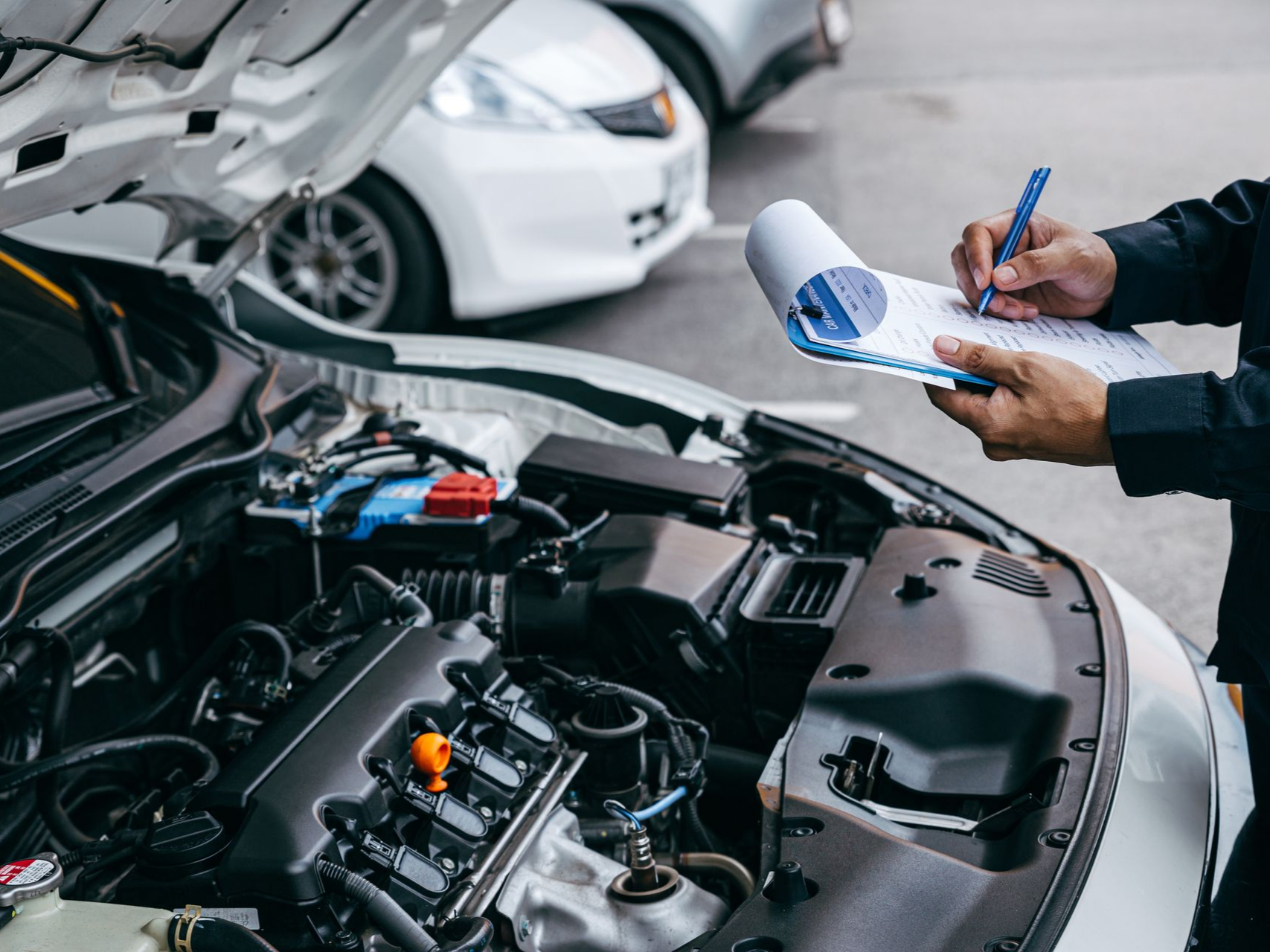 Un mécanicien prend des notes tout en inspectant le moteur ouvert d'une voiture dans un garage.
