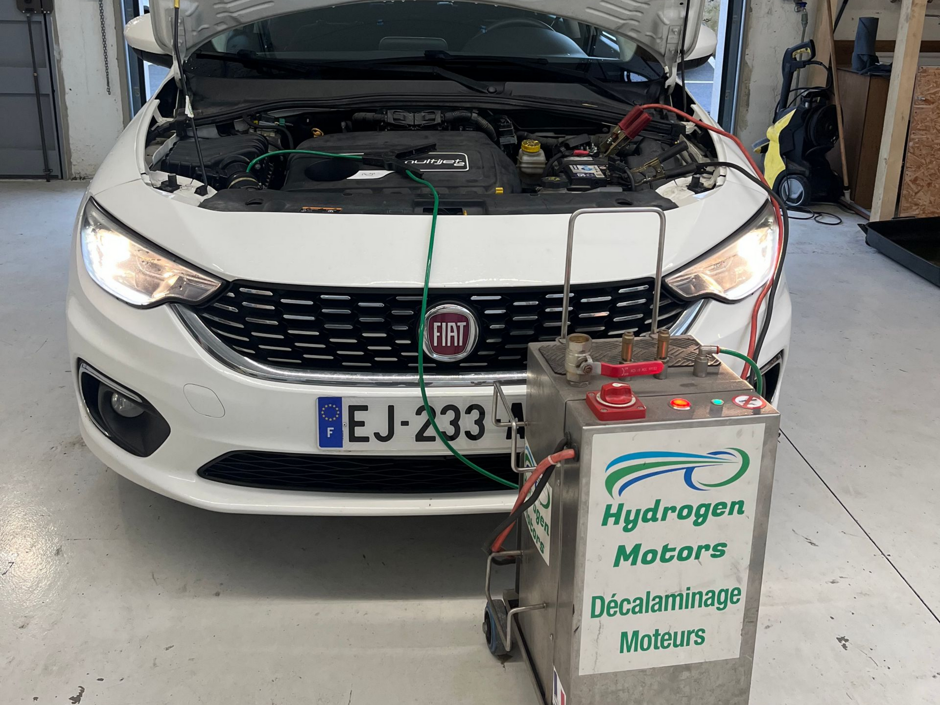 Une Fiat blanche subit un processus de nettoyage du carbone du moteur avec une machine Hydrogen Motors dans un garage.