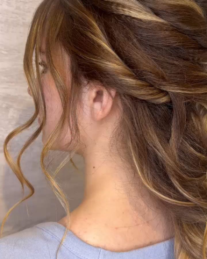 Primer plano de perfil de una melena castaña ondulada con mechas, peinada en un recogido parcial suelto con suaves mechones que enmarcan el rostro.