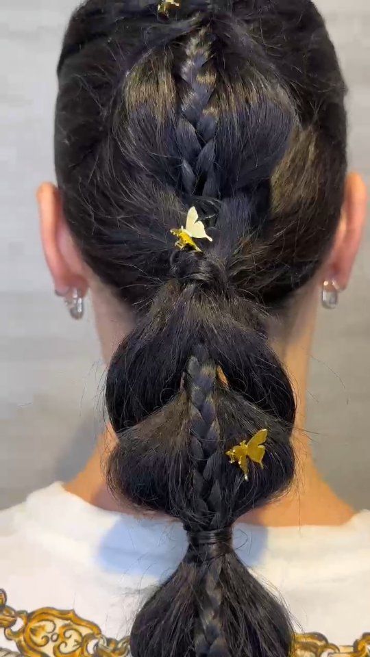 Una persona de cabello oscuro vista de espaldas con un peinado de coleta abullonada, adornado con pequeñas pinzas doradas en forma de mariposa.
