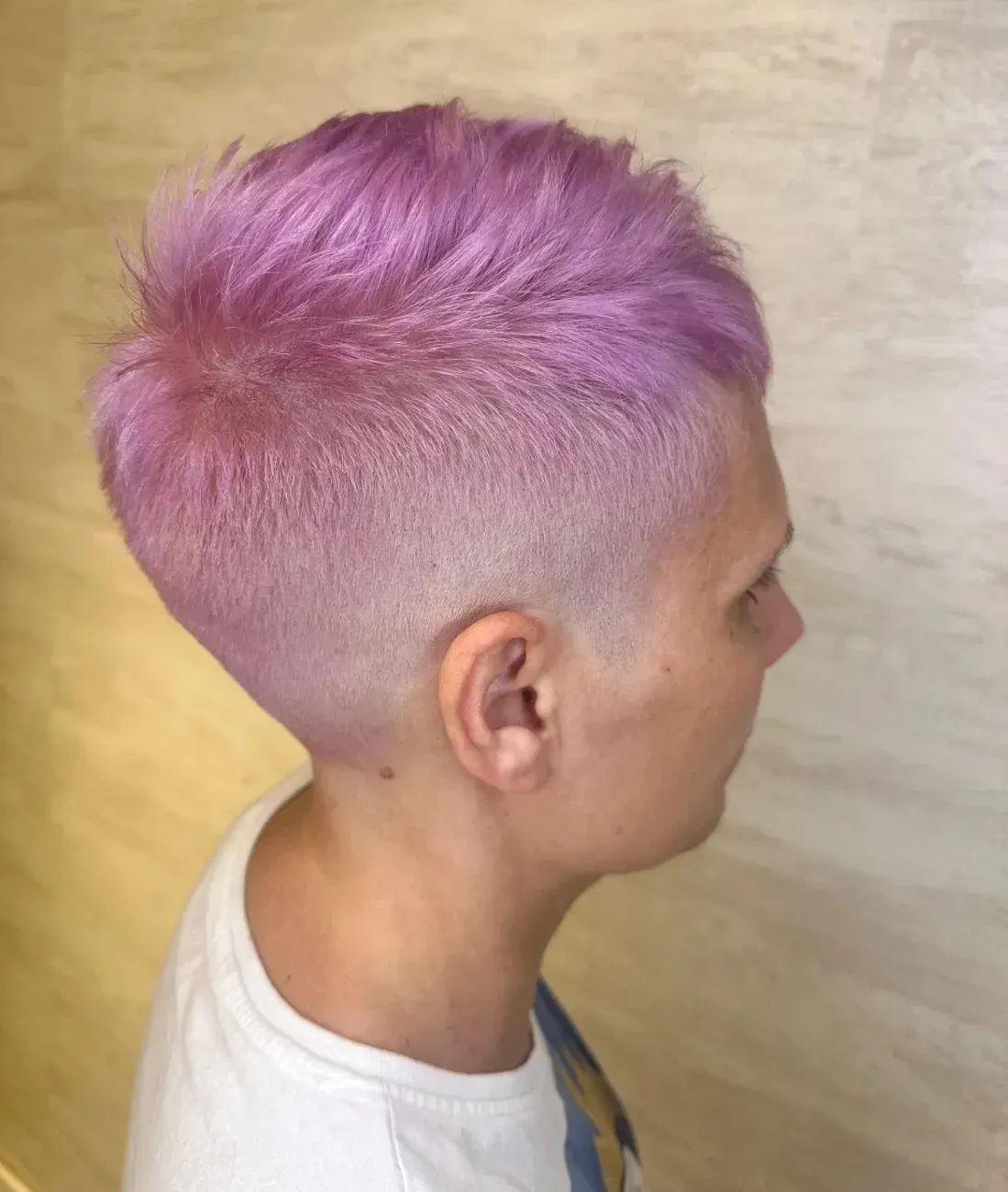Perfil lateral de una persona con un corte de pelo pixie corto de color lavanda descolorido, con los lados rapados y con un degradado muy marcado.