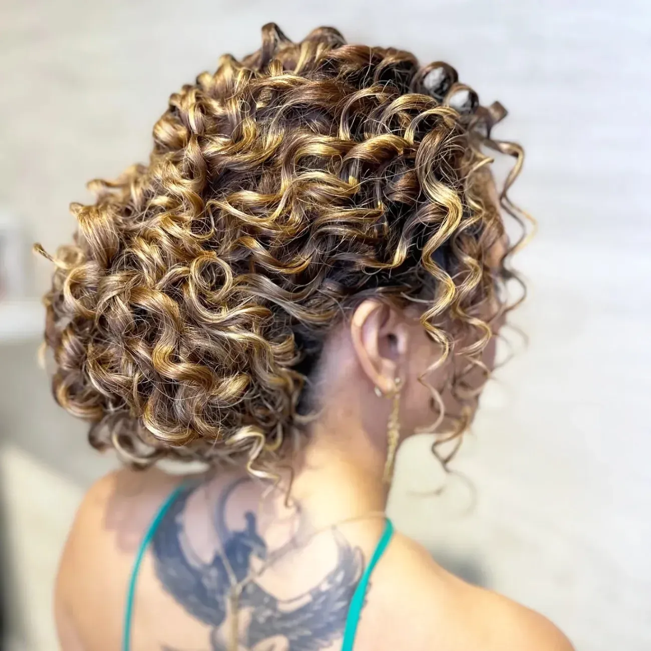 Vista posterior de una persona con cabello rizado, de varios tonos castaños y rubios, peinado en un voluminoso recogido.