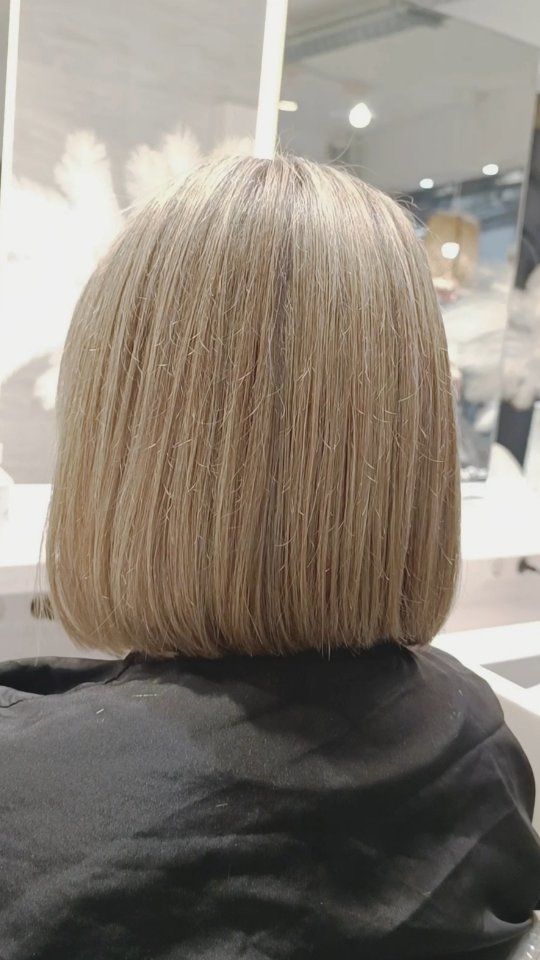 Un corte de pelo bob rubio liso a la altura de los hombros visto desde atrás en un salón de belleza.