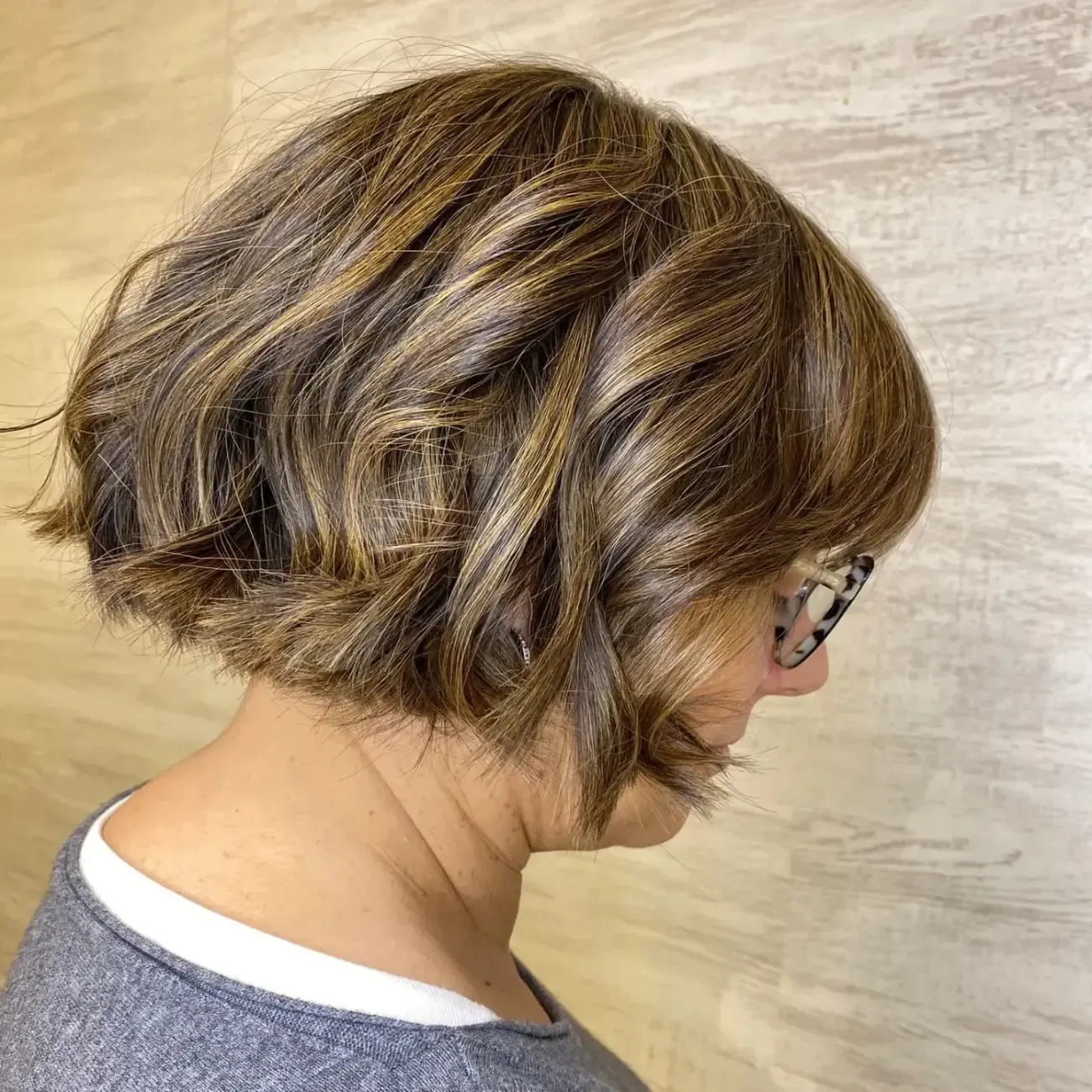 Una persona con cabello corto, ondulado y castaño con mechas, vista de perfil, con gafas y sobre un fondo neutro.