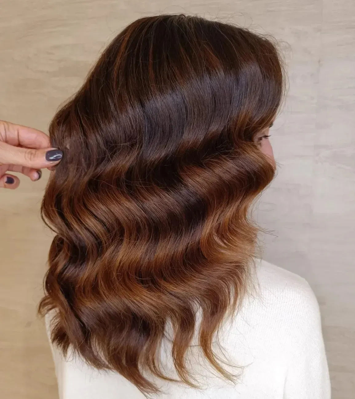 Cabello castaño con ondas suaves y sueltas y sutiles reflejos cálidos, peinado sobre un fondo neutro.