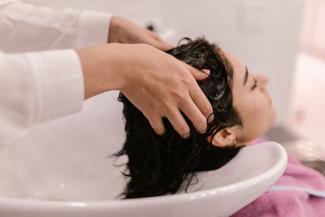Una persona se está lavando el cabello y recibiendo un masaje en el lavabo de una peluquería.