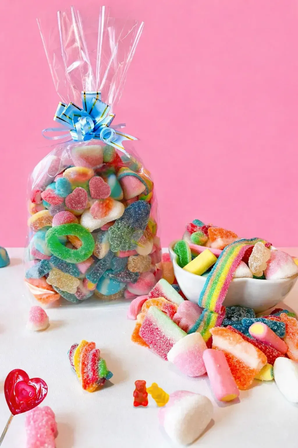 Bolsa de caramelos gomosos de colores atados con una cinta azul, con caramelos esparcidos y un cuenco de caramelos