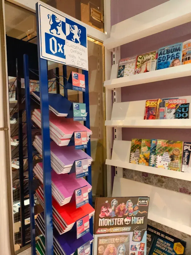 Expositor azul y blanco con cuadernos de colores, junto a un estante con libros en una tienda.