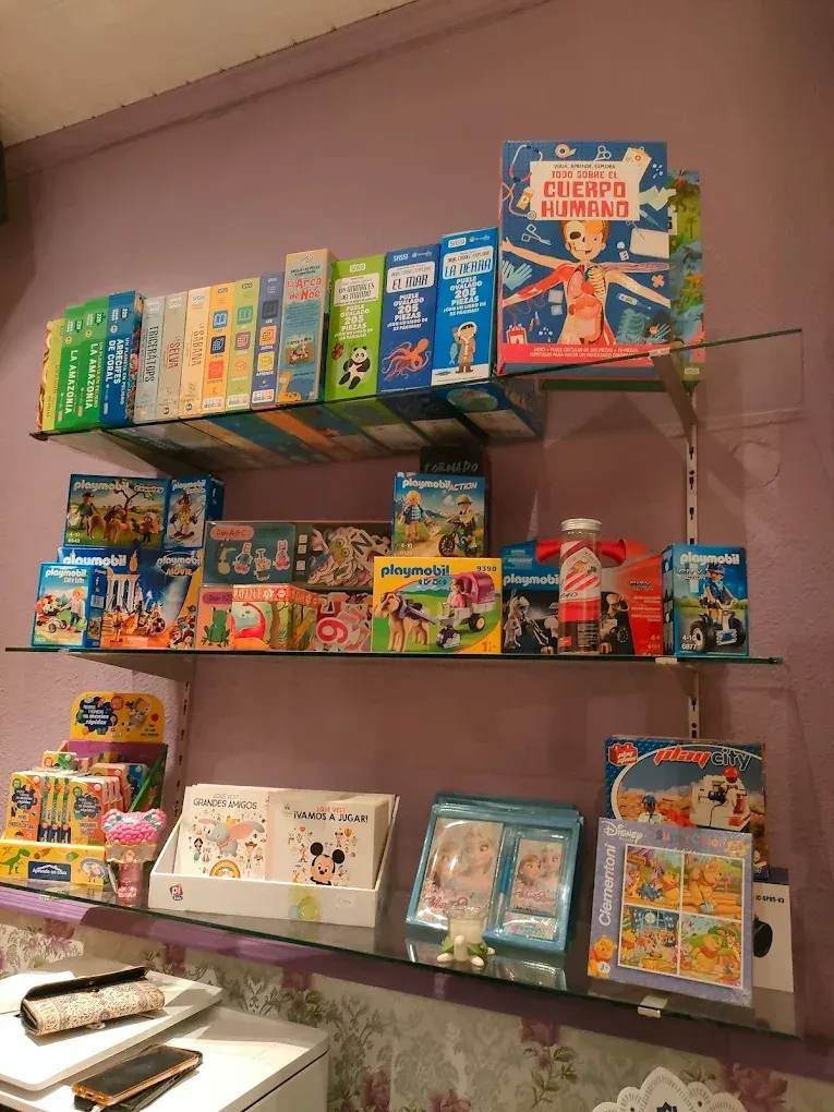 Estanterías con libros infantiles coloridos y juguetes contra una pared violeta.