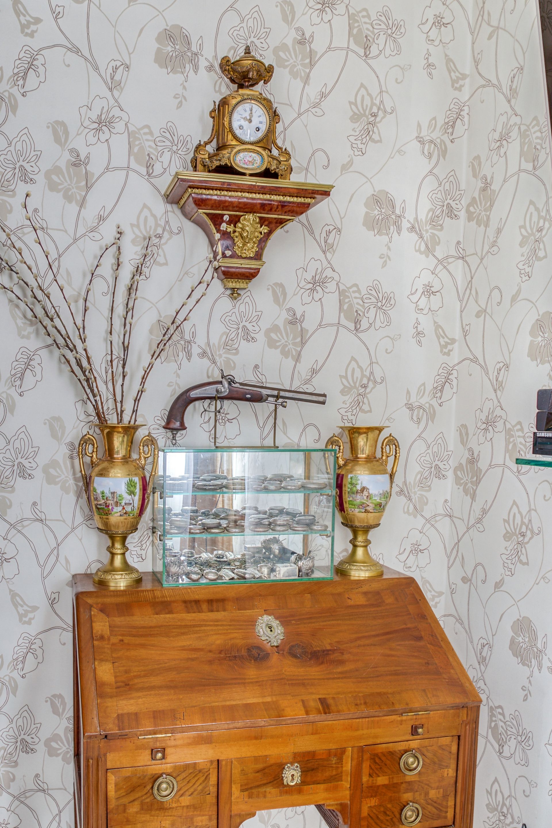 Bureau ancien avec horloge, pistolet, vases et vitrine sur papier peint à motifs